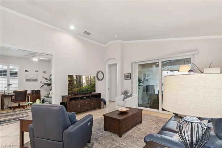 Living room featuring ceiling fan, light tile patterned floors, lofted ceiling, and ornamental molding