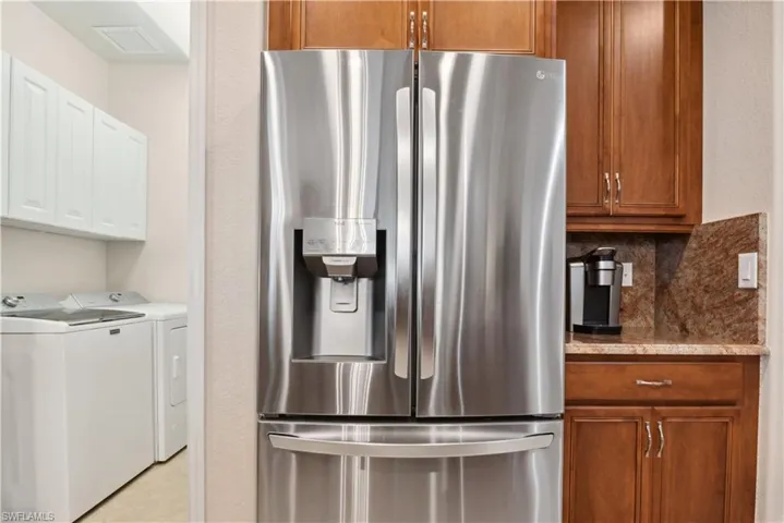 Kitchen featuring tasteful backsplash, stainless steel fridge with ice dispenser, light tile patterned floors, and independent washer and dryer
