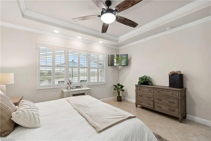Bedroom featuring a raised ceiling, ceiling fan, light tile patterned floors, and ornamental molding