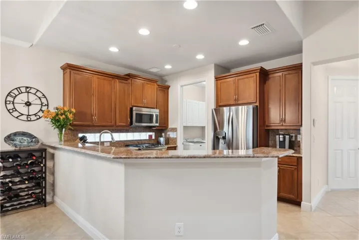 Kitchen featuring light stone countertops, appliances with stainless steel finishes, tasteful backsplash, light tile patterned flooring, and kitchen peninsula