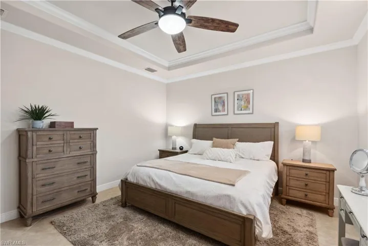 Tiled bedroom featuring a raised ceiling, ceiling fan, and crown molding