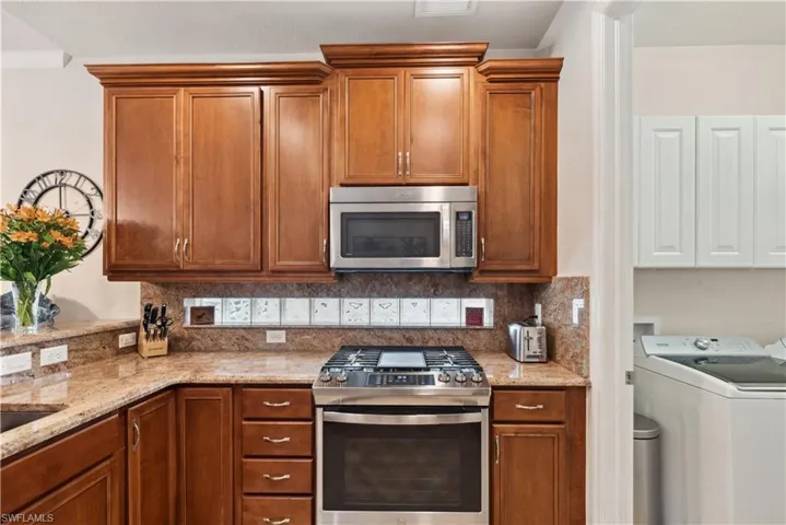 Kitchen featuring light stone countertops, washer / dryer, stainless steel appliances, and tasteful backsplash