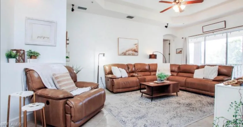 Tiled living room featuring a tray ceiling, arched walkways, and ceiling fan