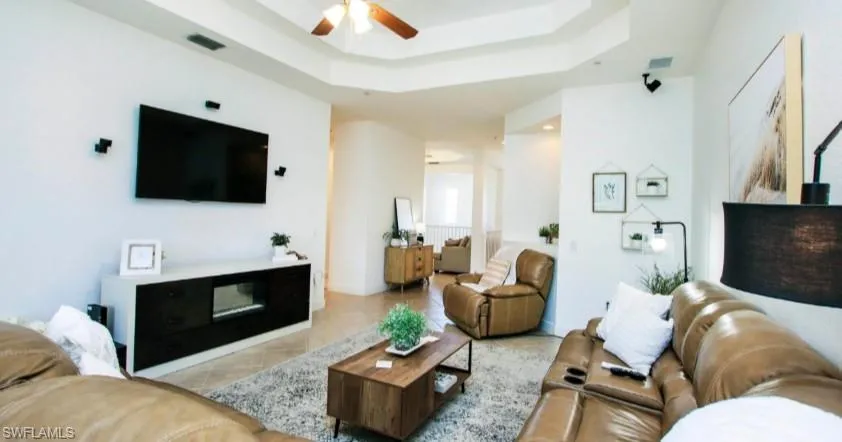 Living area featuring a tray ceiling, a ceiling fan, and tile patterned floors