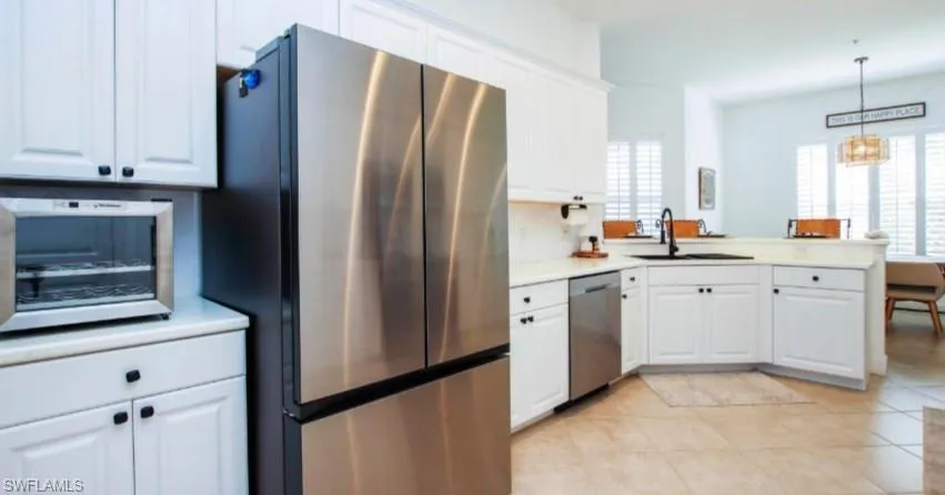 Kitchen featuring stainless steel appliances, white cabinets, light countertops, and a peninsula