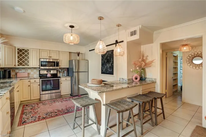 Kitchen featuring appliances with stainless steel finishes, light tile patterned flooring, a peninsula, ornamental molding, and a kitchen breakfast bar- Virtually Edited Image