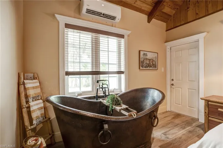 Bedroom area featuring a wall mounted air conditioner, wood finished floors, and wood ceiling- Virtually Edited Image