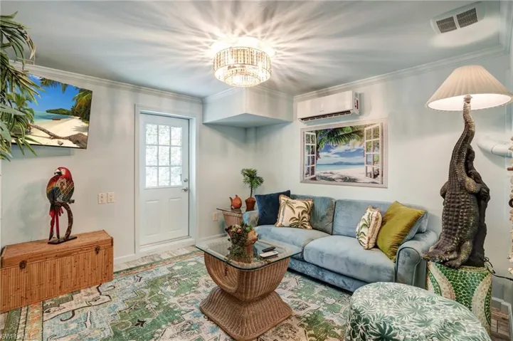 Living area with an AC wall unit, a chandelier, baseboards, and ornamental molding- Virtually Edited Image