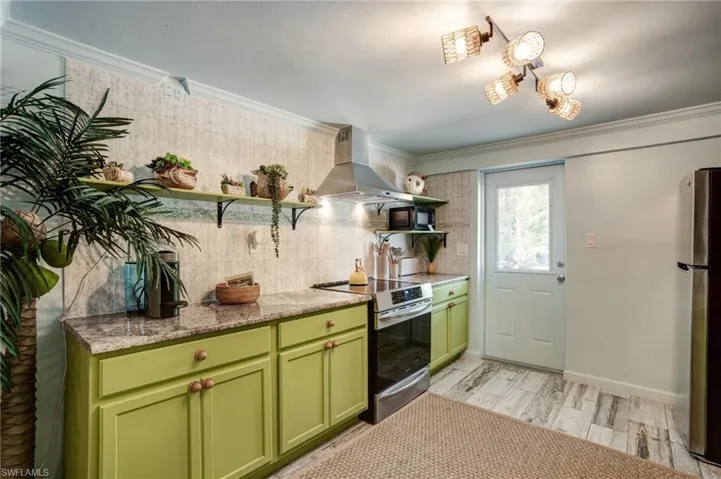 Kitchen with green cabinetry, open shelves, stainless steel appliances, wall chimney range hood, and tasteful backsplash- Virtually Edited Image