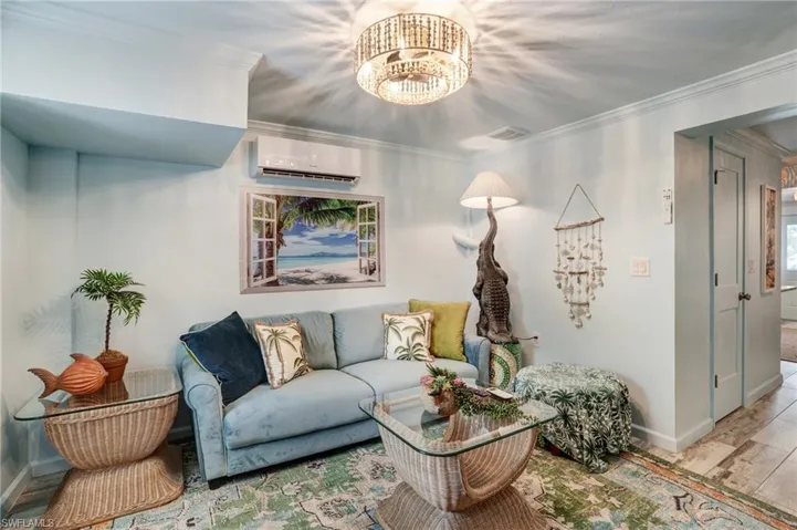 Living room featuring a wall mounted air conditioner, baseboards, a chandelier, ornamental molding, and wood finished floors- Virtually Edited Image
