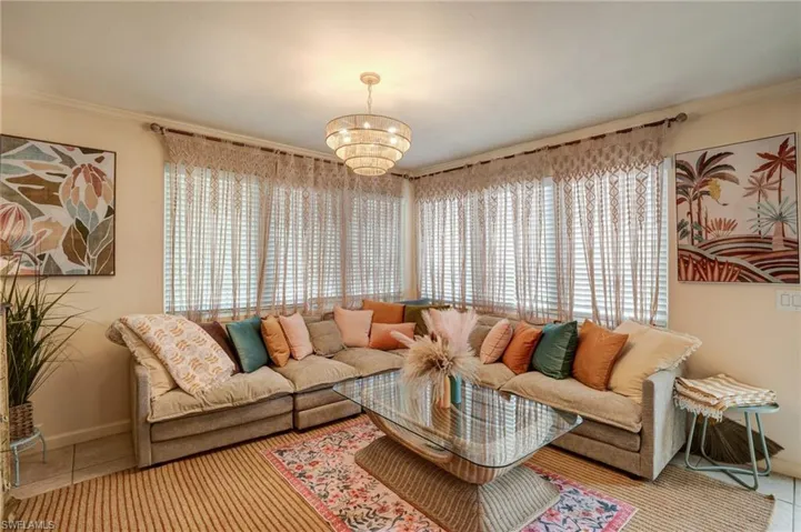 Living area with a chandelier, plenty of natural light, crown molding, tile patterned flooring, and baseboards- Virtually Edited Image
