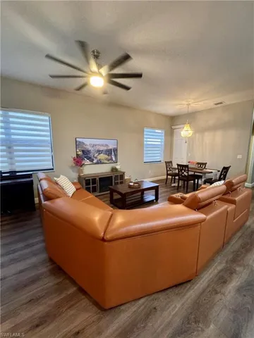 Open-concept living space featuring wood-finish flooring, a contemporary ceiling fan, and multiple windows with horizontal blinds