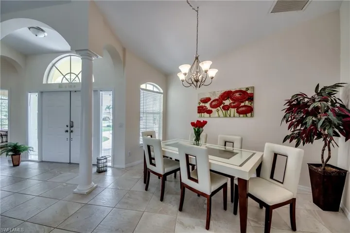 Dining room featuring high vaulted ceiling, decorative columns, arched walkways, a chandelier, and light tile patterned floors
