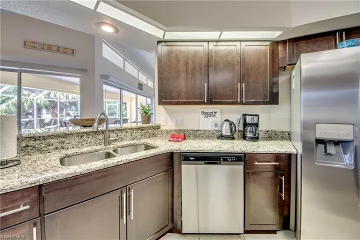 Kitchen with stainless steel appliances, light stone counters, dark brown cabinets, and light tile patterned floors