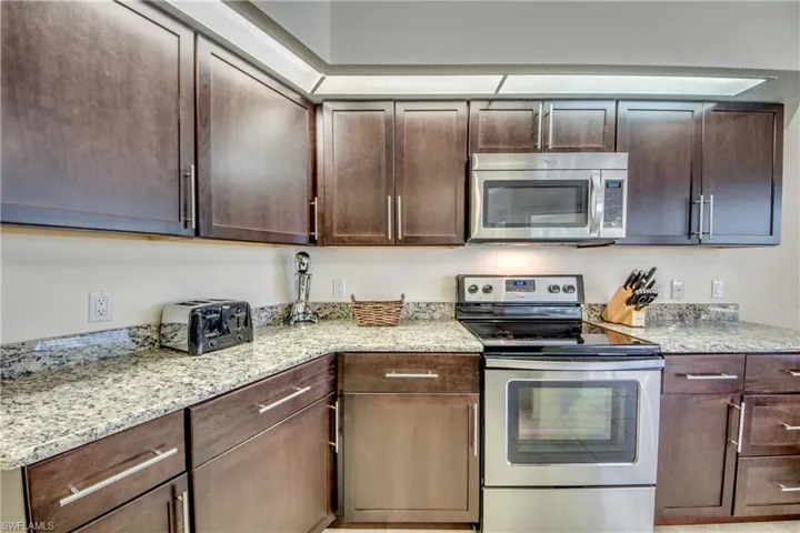 Kitchen with stainless steel appliances, light stone counters, and dark brown cabinets
