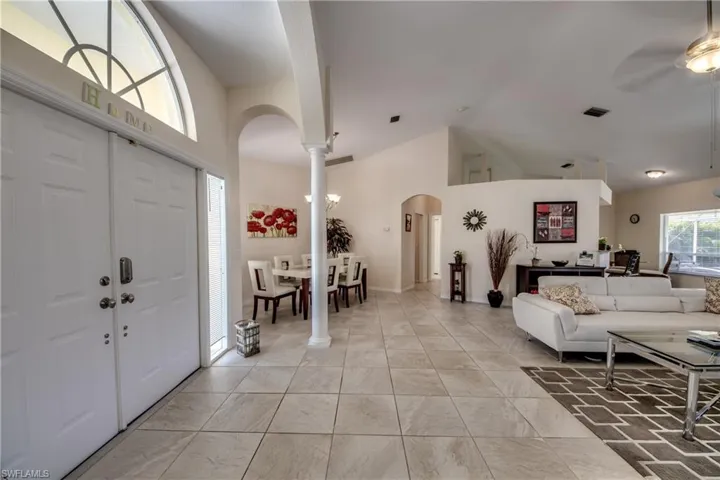 Entryway featuring arched walkways, ceiling fan, high vaulted ceiling, decorative columns, and light tile patterned flooring