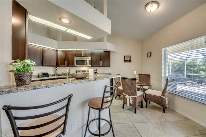 Kitchen with dark brown cabinetry, light stone countertops, a breakfast bar, stainless steel microwave, and light tile patterned floors