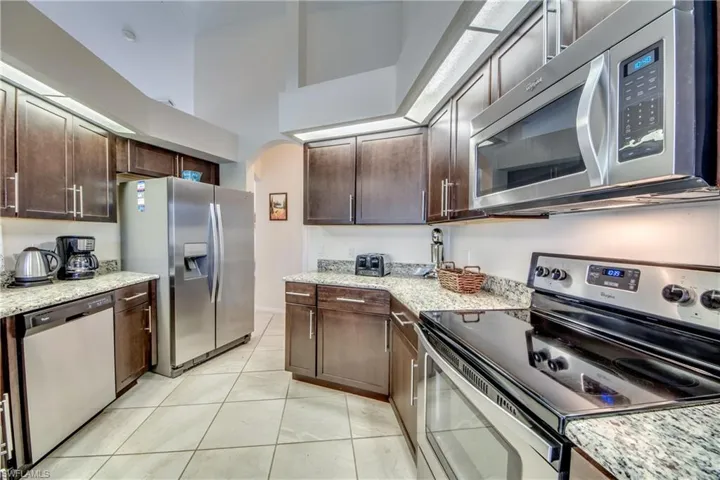 Kitchen featuring stainless steel appliances, dark brown cabinetry, and light stone counters