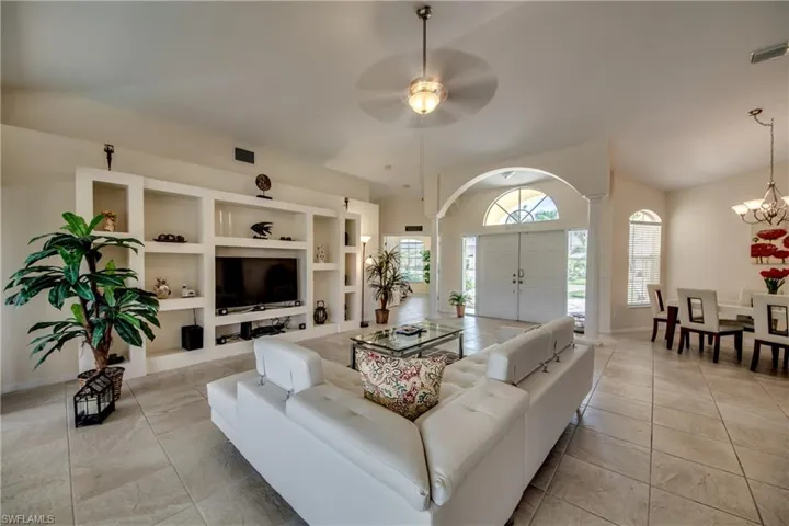 Living area featuring a ceiling fan, built in shelves, light tile patterned floors, and a chandelier