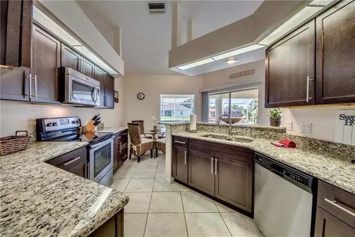 Kitchen featuring stainless steel appliances, dark brown cabinetry, light tile patterned flooring, light stone countertops, and a peninsula