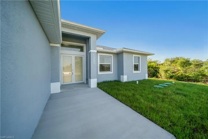 Property entrance with french doors, stucco siding, and a lawn