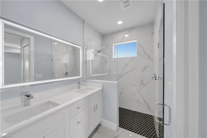 Bathroom featuring double vanity, a marble finish shower, a sink, and visible vents