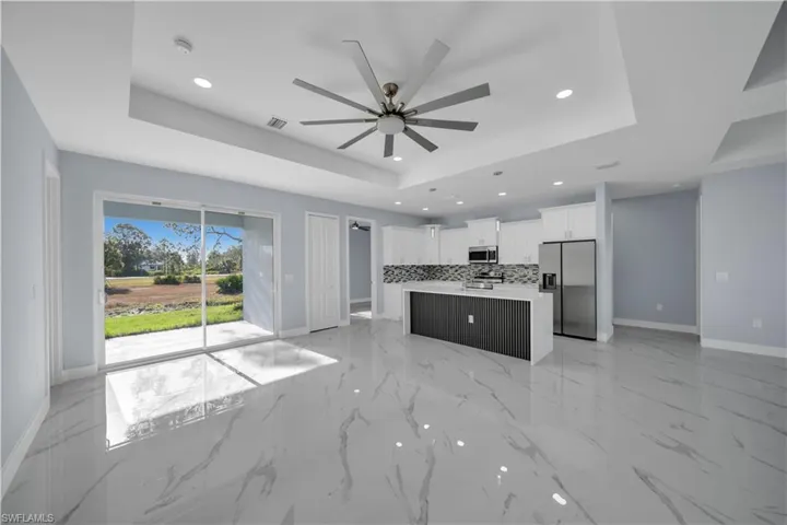 Kitchen featuring baseboards, a raised ceiling, ceiling fan, stainless steel appliances, and decorative backsplash
