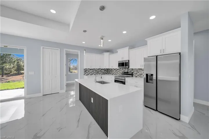 Kitchen featuring tasteful backsplash, baseboards, white cabinetry, appliances with stainless steel finishes, and a sink