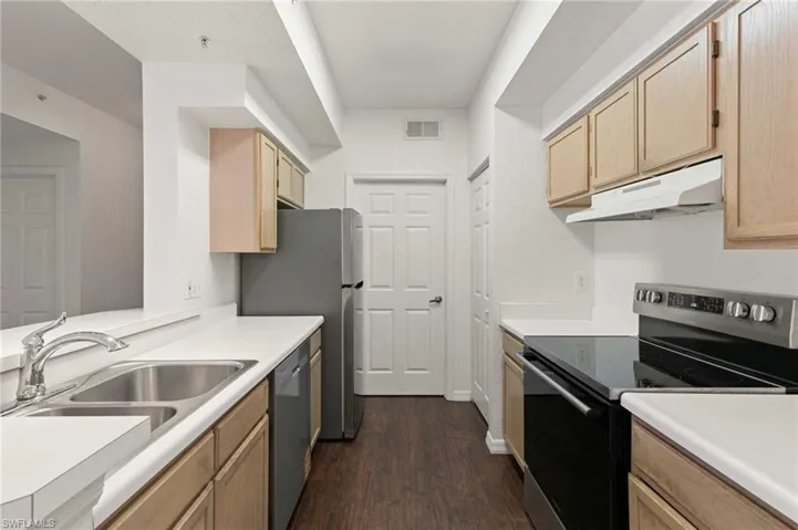 Kitchen with appliances with stainless steel finishes, under cabinet range hood, light brown cabinetry, dark wood-type flooring, and light countertops