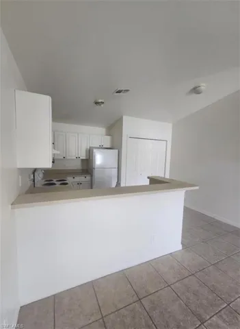 Kitchen with white appliances, light countertops, a peninsula, white cabinets, and light tile patterned flooring