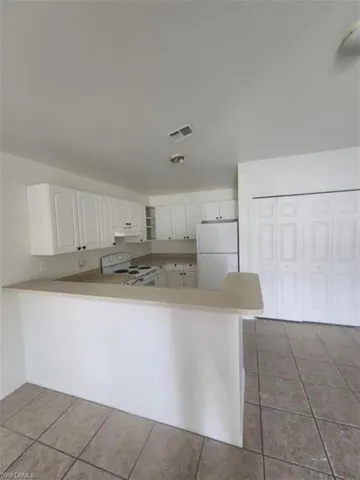 Kitchen with white appliances, light tile patterned flooring, a peninsula, and light countertops
