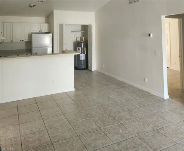 Kitchen with freestanding refrigerator, white cabinets, electric water heater, light tile patterned flooring, and a peninsula