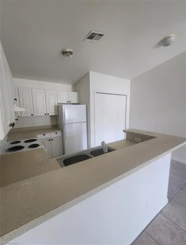 Kitchen with white appliances, light countertops, light tile patterned floors, white cabinetry, and a peninsula
