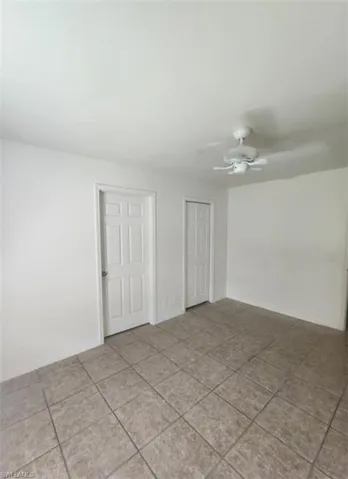 Tiled empty room featuring a ceiling fan and baseboards