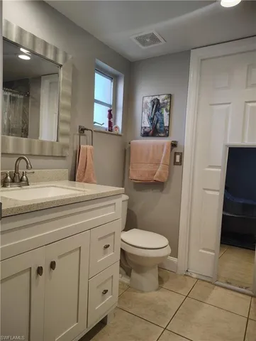 Bathroom with toilet, tile patterned flooring, visible vents, and vanity