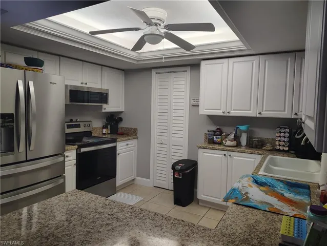 Kitchen with appliances with stainless steel finishes, white cabinetry, ceiling fan, and light tile patterned floors