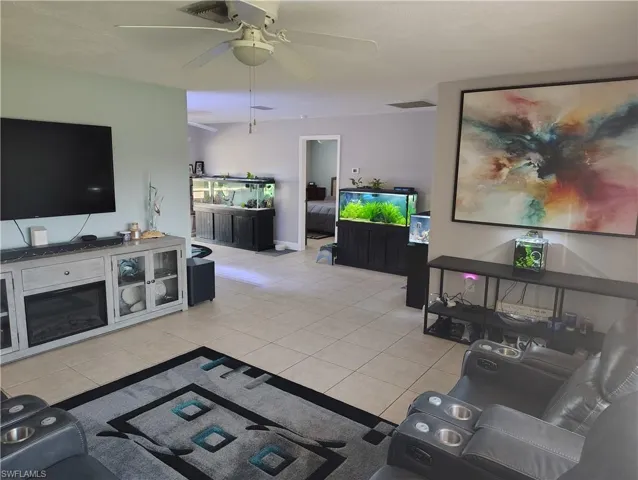 Living area with a ceiling fan, light tile patterned flooring, and visible vents