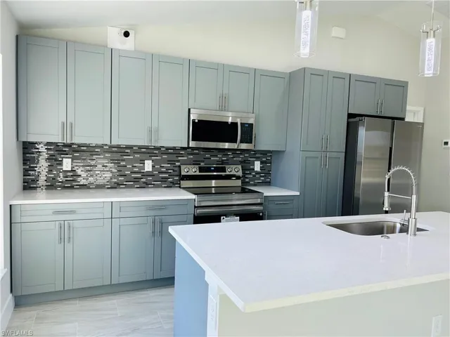Kitchen featuring lofted ceiling, tasteful backsplash, appliances with stainless steel finishes, pendant lighting, and sink