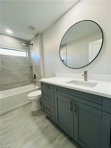 Full bathroom with vanity, tiled shower / bath combo, and toilet