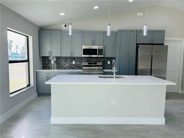 Kitchen with sink, stainless steel appliances, vaulted ceiling, and a center island with sink