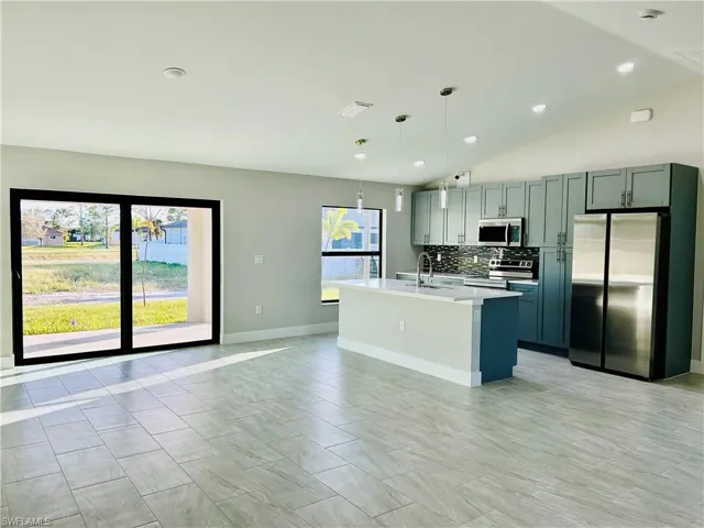 Kitchen featuring hanging light fixtures, a center island with sink, vaulted ceiling, and appliances with stainless steel finishes