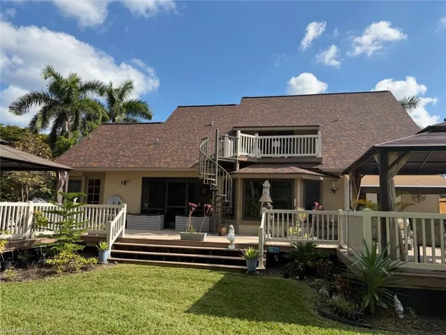 Rear exterior featuring a multi-level deck, spiral staircase, upper-level balcony with white railings, and a brown shingle roof