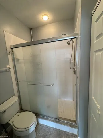 Bathroom with tile patterned floors, a shower with door, and toilet