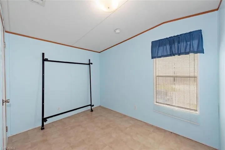 Unfurnished bedroom featuring ornamental molding, vaulted ceiling, and light floors