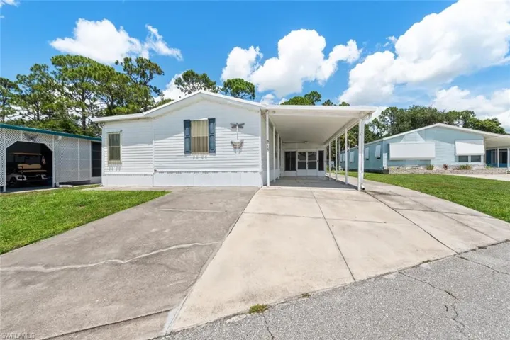 Manufactured / mobile home featuring concrete driveway, a front lawn, and an attached carport