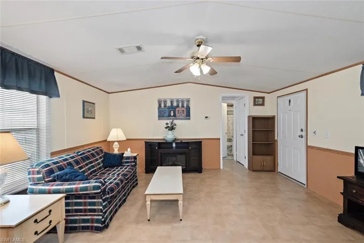 Living area with ornamental molding, lofted ceiling, a ceiling fan, and light floors