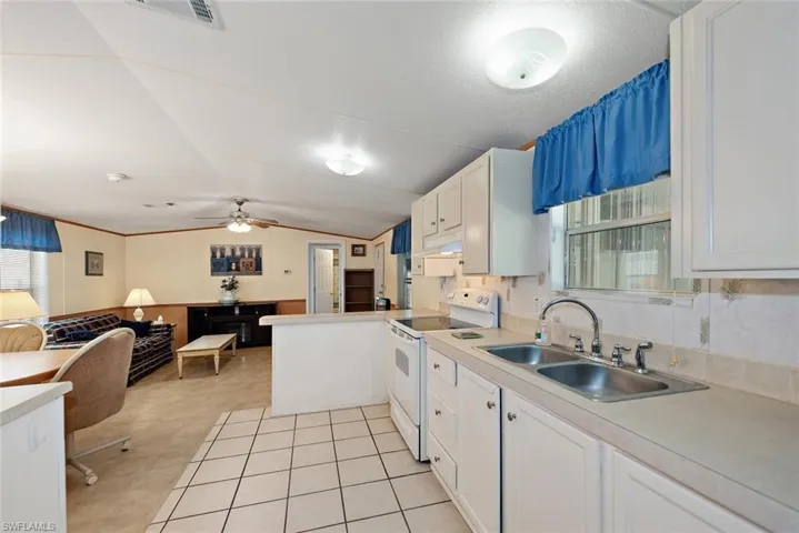 Kitchen featuring white electric range, light countertops, lofted ceiling, white cabinets, and a ceiling fan