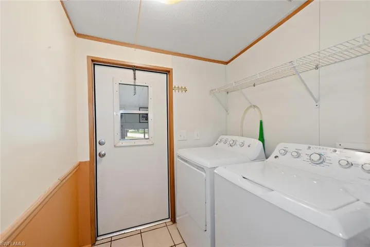 Laundry area with washing machine and dryer, ornamental molding, and light tile patterned floors