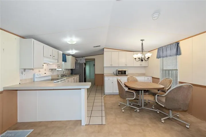 Kitchen with appliances with stainless steel finishes, light countertops, lofted ceiling, a chandelier, and a peninsula