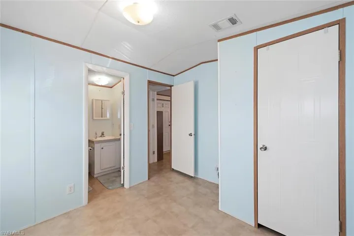 Unfurnished bedroom featuring light floors, vaulted ceiling, and ensuite bath